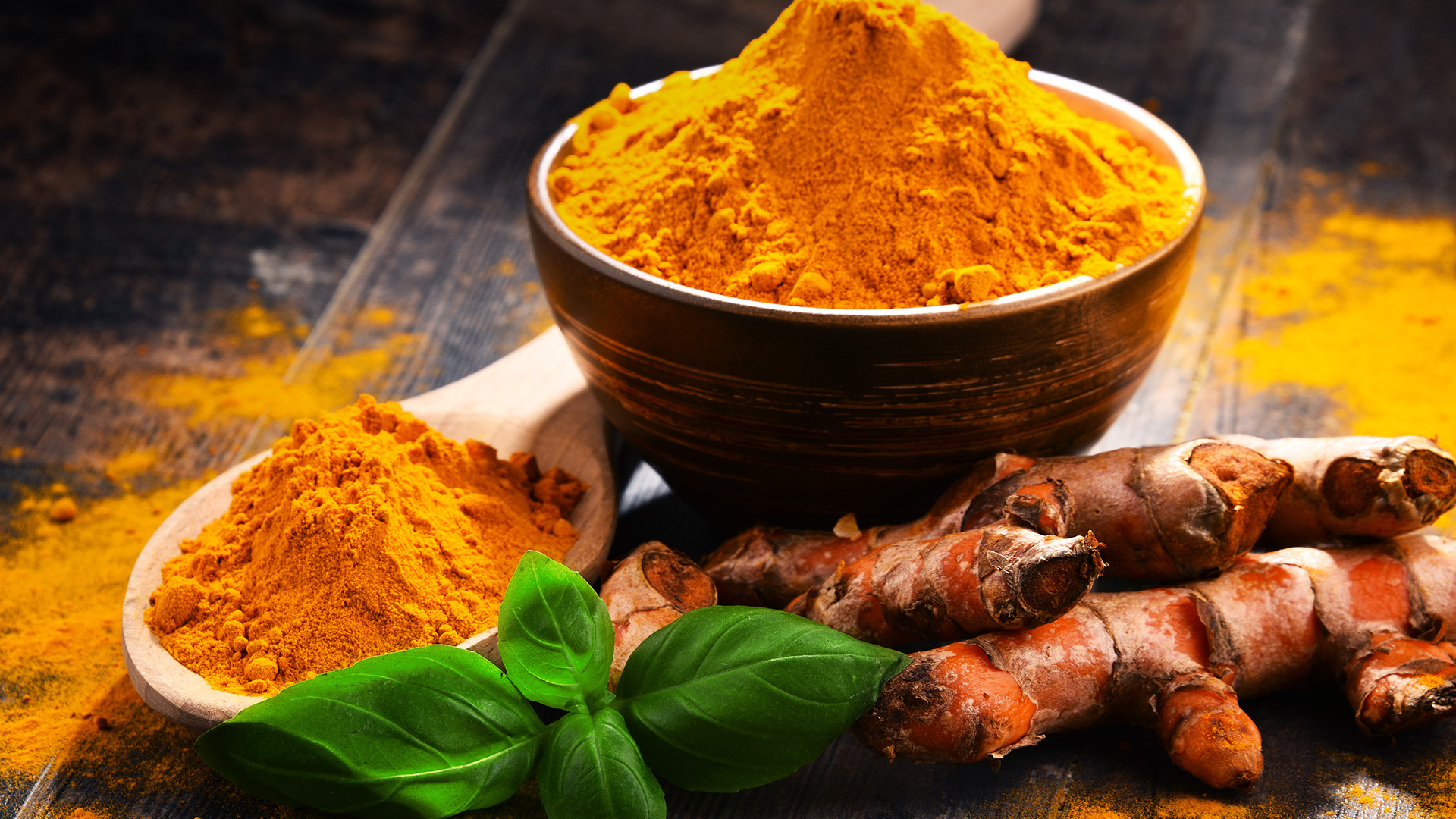 Composition with bowl of turmeric powder and turmeric root on wooden table. What are the benefits of turmeric?