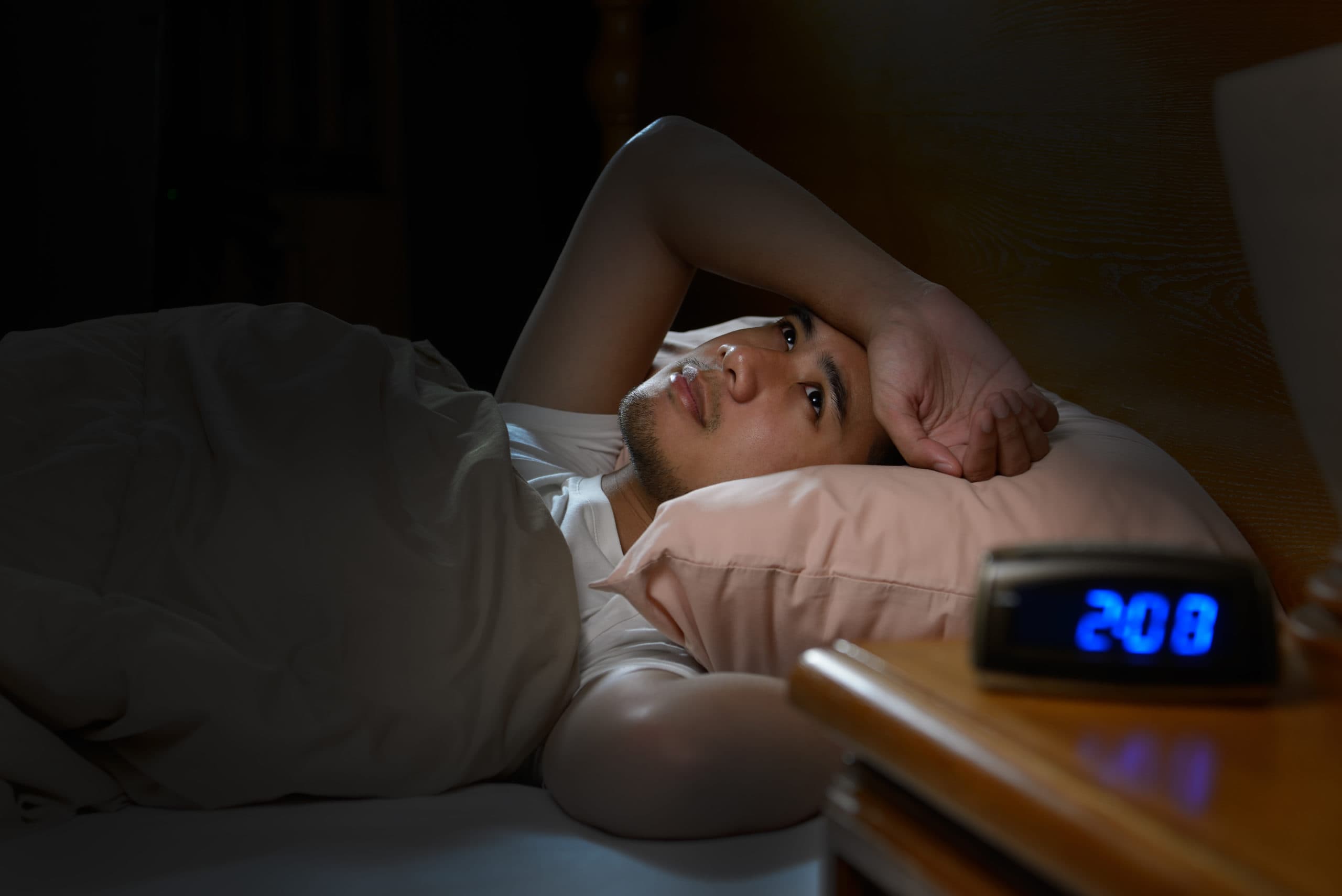 man laying awake in bed as the clock reads 2:08am and he is wondering what to do when you can't sleep