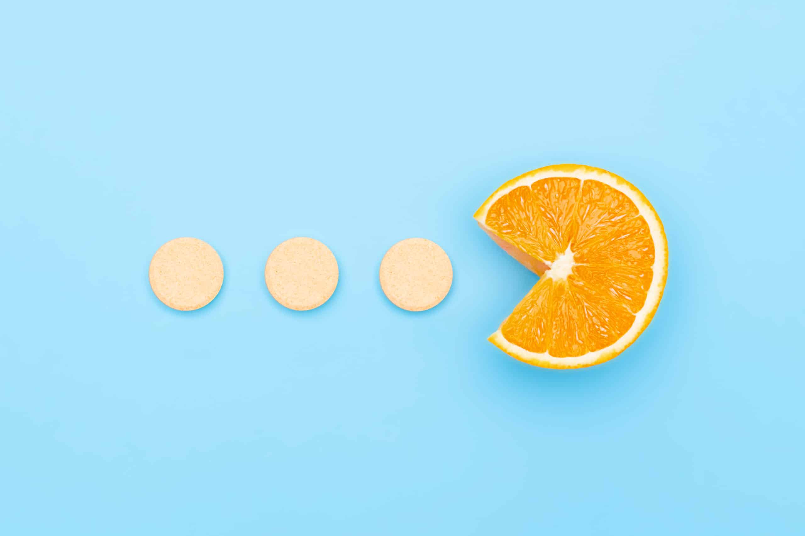 Vitamin C supplements pills with Orange Fruit Cross Section isolated on blue background. Vitamin deficiency, avitaminosis concept. Homeopathy cure treatment, to show how much vitamin c when sick should i take