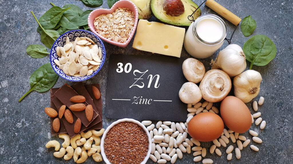 A chalkboard with the periodic table element sign for zinc written on it, surrounded by foods naturally containing zinc such as nuts, vegetables, and dairy - best zinc supplements.