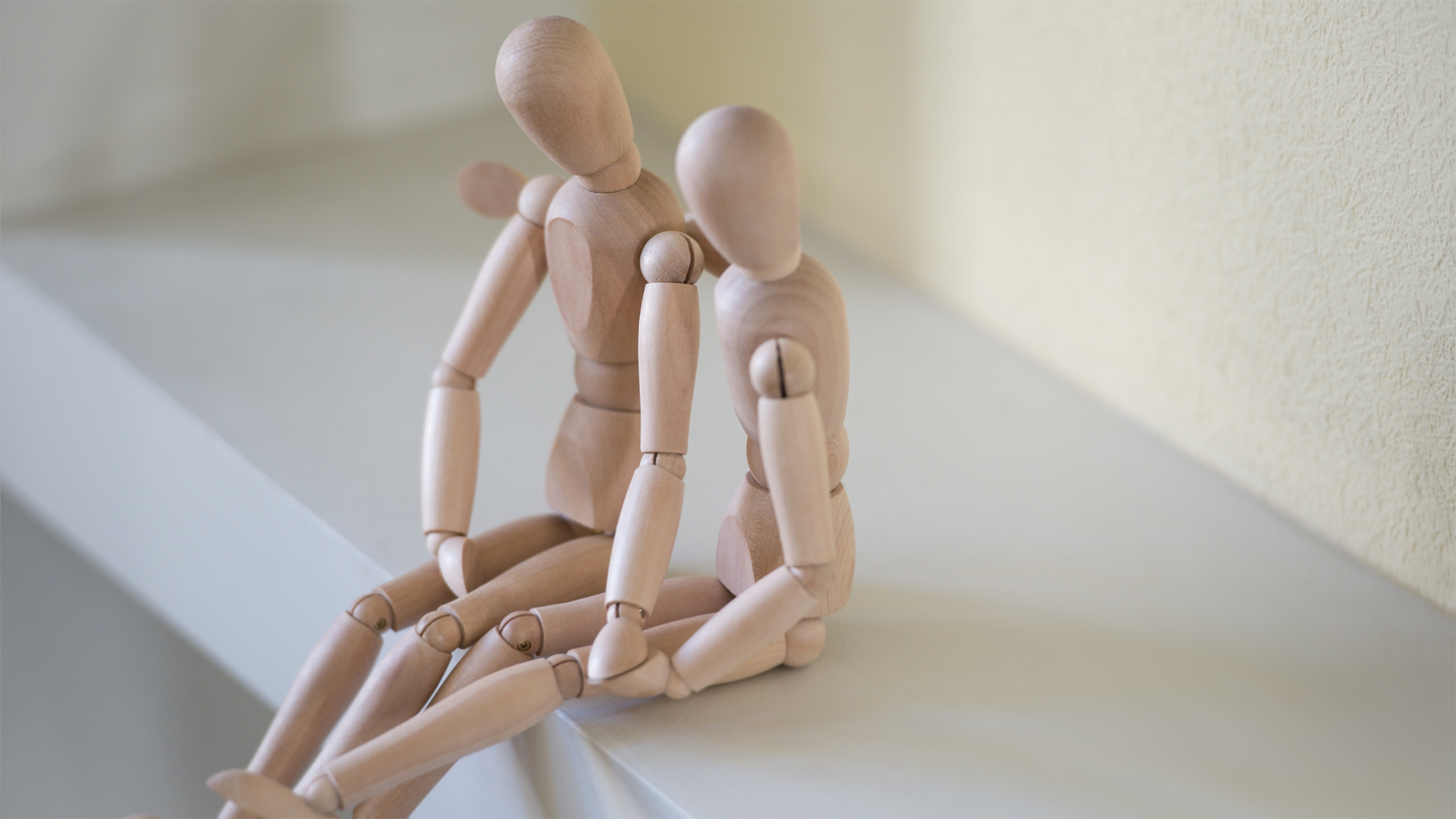 Two artist mannequins posed to show that one is comforting the other with its arm around the second mannequin's shoulder, both sitting on a white shelf, representing Healthy Communication in Relationships.