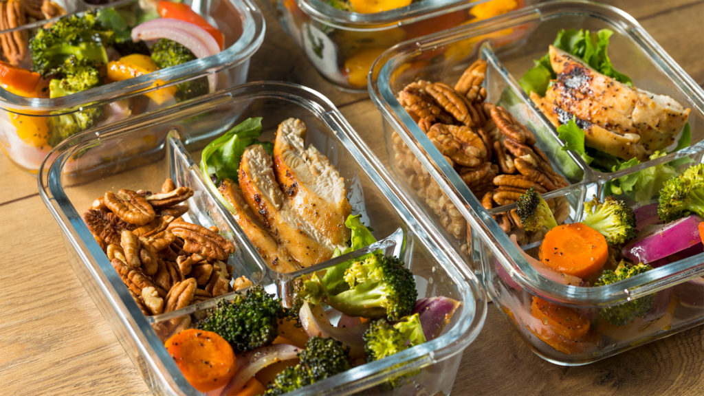 A delicious pre-portioned meal in glass container, with chicken, vegetables, and some nuts, exemplifying how to meal prep effectively and still eat great.