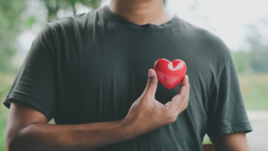 A man wearing a t-shirt holding a red heart-shaped object to his chest where his heart would be, illustrating support for heart health.